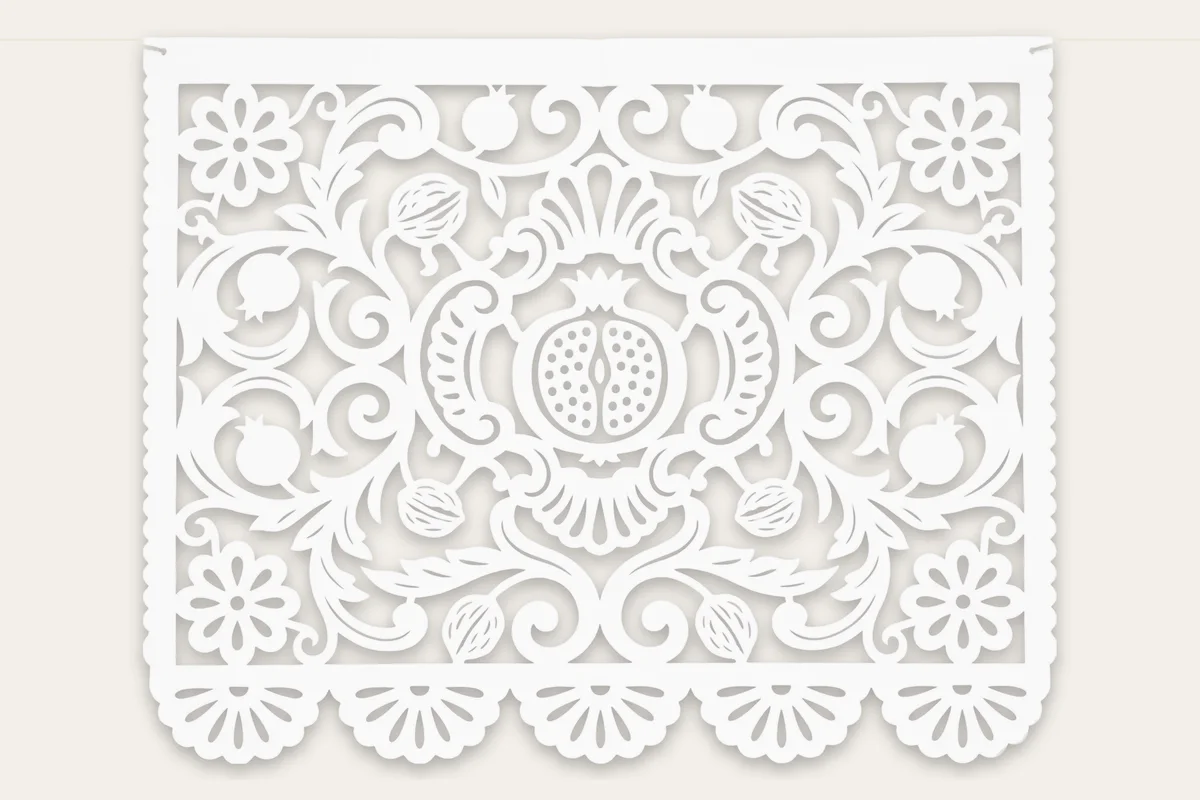 La misma pieza barroca de granada, acanto y nueces cortada en papel picado blanco, el color de la nogada