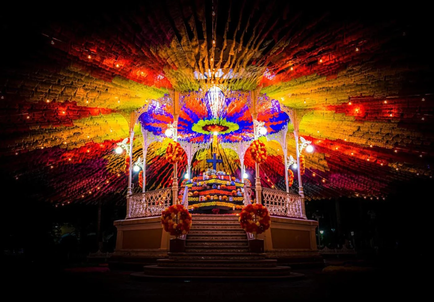 Kiosco iluminado con dosel de papel picado creando explosión de color nocturna
