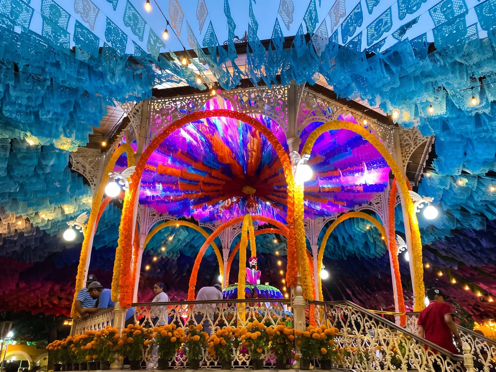 Kiosco con dosel de papel picado en tonos turquesa y azul, iluminado de noche