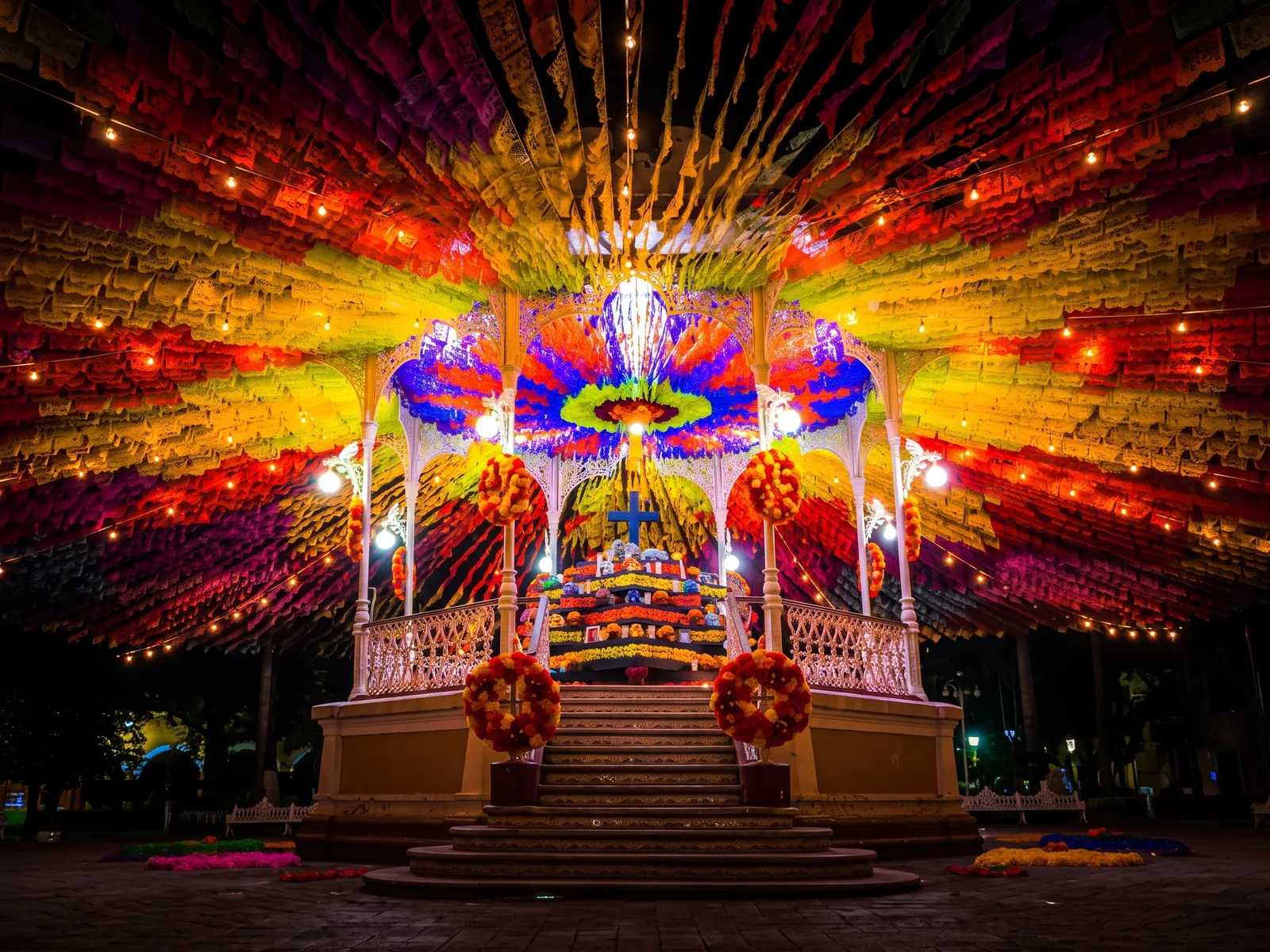 Kiosco iluminado de noche bajo un dosel de papel picado multicolor