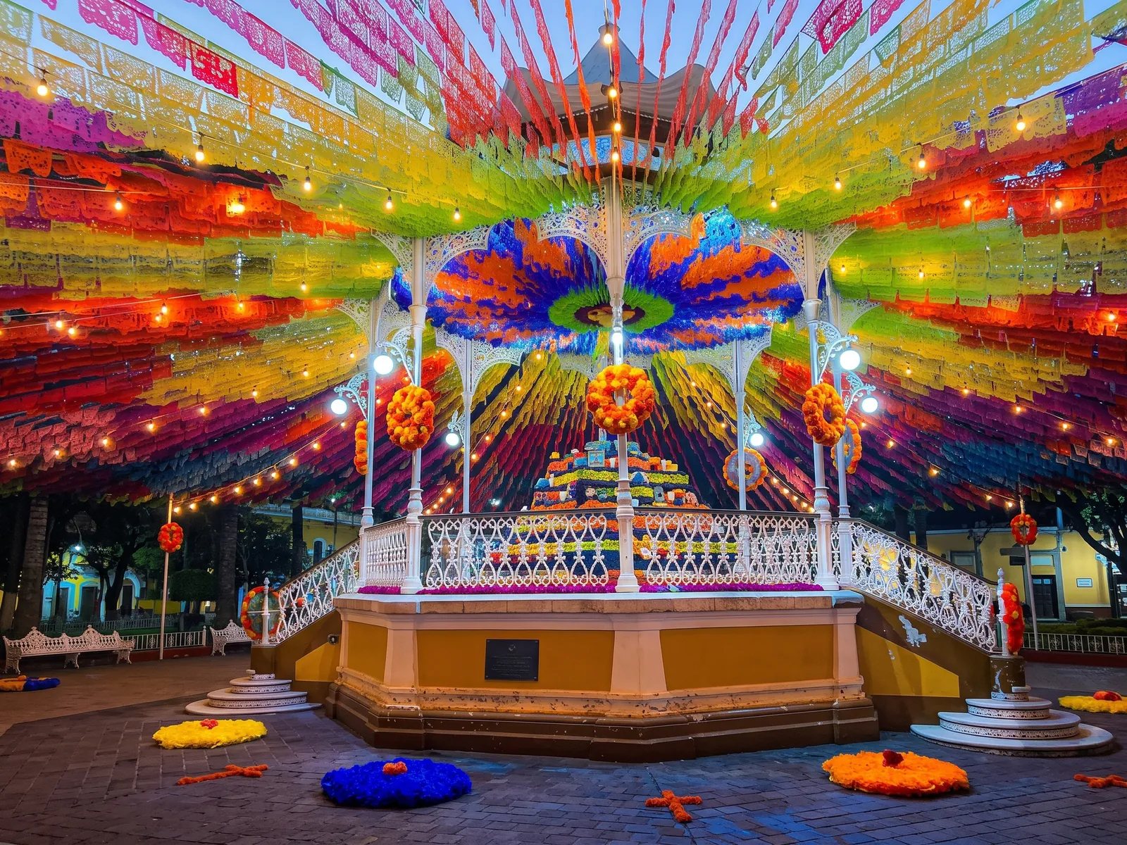 Kiosco decorado con un techo de papel picado de colores para una fiesta patronal